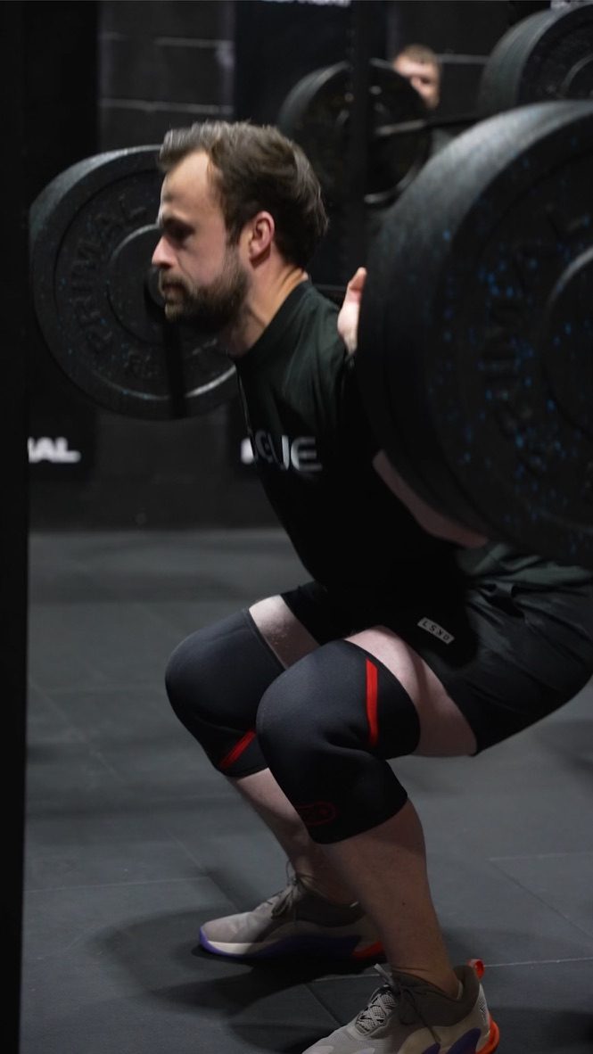 Member back squatting with a coach watching